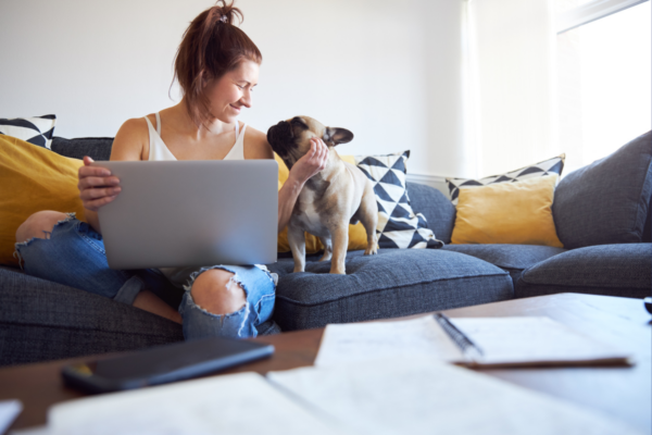 A woman and a dog looking at each other on a blue couch. The woman has a computer on her lap.